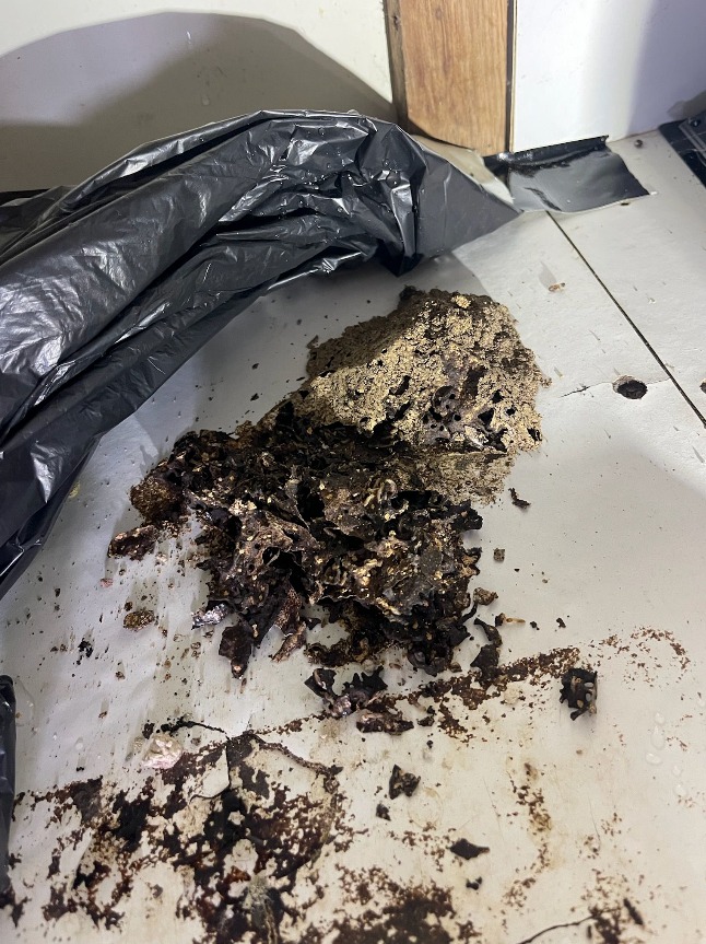 A dirty floor with a trash bag and a piece of wood in the background.