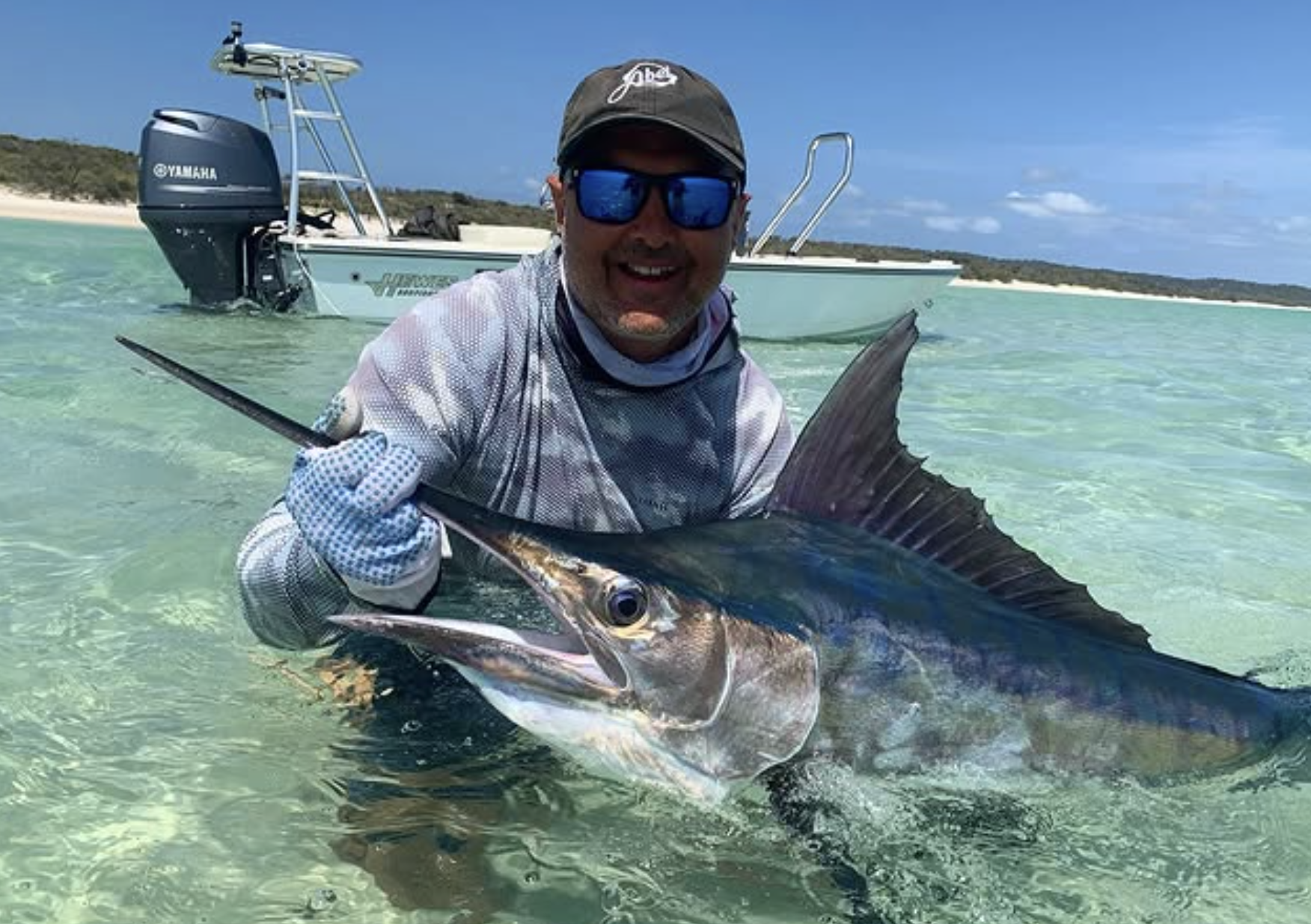 Shannon in a boat holds a large marlin in shallow water.