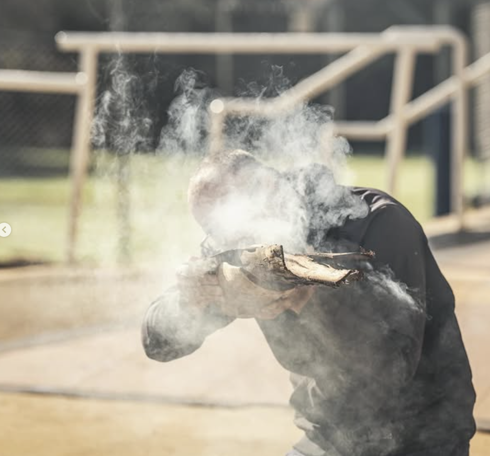 Shannon Kitchener in a black shirt holds a smoldering log, with smoke rising from it.